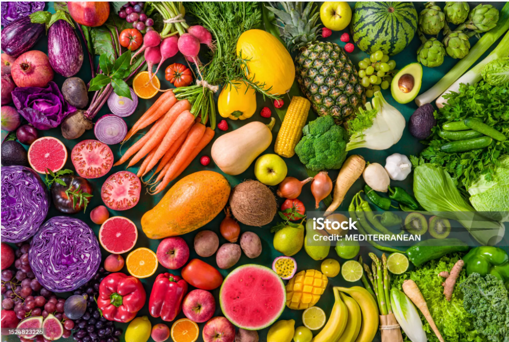 An assortment of fresh fruits and vegetables, including carrots, grapes, watermelon, pineapple, avocado, bananas, and various leafy greens, arranged in a colorful display.