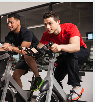 Two men exercising on stationary bikes in a gym, focusing on cardiovascular training and endurance building.