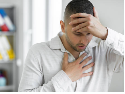 A man experiencing symptoms of anxiety, holding his chest with one hand and his forehead with the other, appearing distressed and overwhelmed.